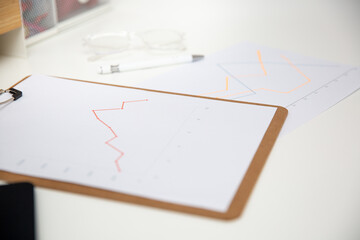 Office workplace table with charts report on wooden clipboard, glasses and pen.