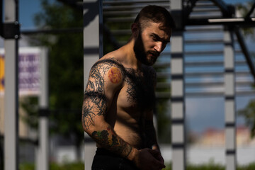 The young guy trains in the park on the street exercise machine