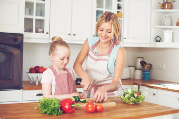 Mother, kid and preparing a salad in home with cutting ingredients, nutrition meal and teaching healthy vegan recipe. Woman, girl and learning to cook with support, helping hand or bonding in kitchen