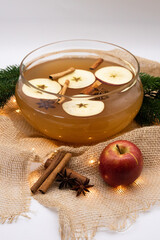 A bowl of clear apple punch with cinnamon sticks, apple slices and star anise floating in it