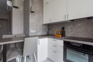 Clean kitchen in a small cozy contemporary studio apartment. Table and chairs in the foreground. Built in household appliance