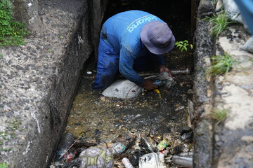 a group of men cleaning the gutter sewage water draining out from cement drain pipe into the...
