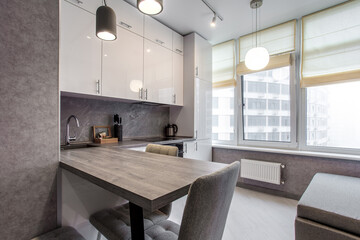 Clean kitchen in a small cozy contemporary studio apartment. Table and chairs in the foreground. Built in household appliance