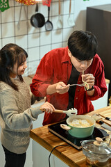 Young couple tasting freshly cooked pasta in a warm Christmas kitchen