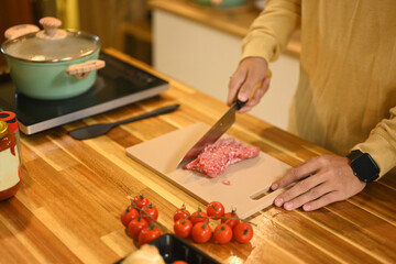 Young man chopping meat on kitchen counter with fresh ingredients