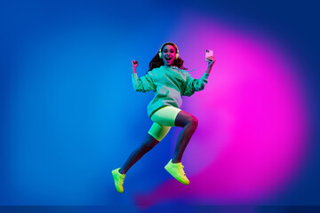 Obraz premium Full length photo of charming positive woman wear sweatshirt headphones jumping winning game device isolated neon blue color background