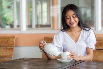 Young Asian Woman Enjoying Tea with a Warm Smile at Cozy Cafe