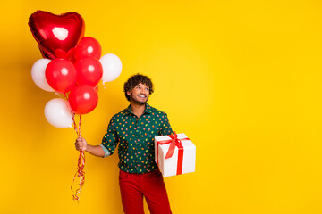 Photo of attractive elegant young man giftbox balloons look empty space wear shirt isolated on yellow color background