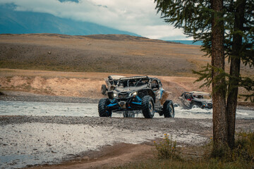 Buggy trip in a Altai desert. Mountain landscape with hills and beautiful blue sky with clouds in background. Off-road vehicles driving on a dust dirt road. Active leisure in Altai Republic. © VaLife