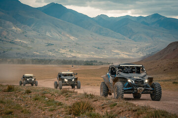 Buggy trip in a Altai desert. Mountain landscape with hills and beautiful blue sky with clouds in background. Off-road vehicles driving on a dust dirt road. Active leisure in Altai Republic. © VaLife