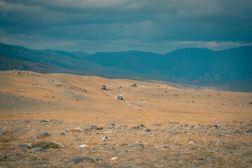Buggy trip in a Altai desert. Mountain landscape with hills and beautiful blue sky with clouds in background. Off-road vehicles driving on a dust dirt road. Active leisure in Altai Republic.