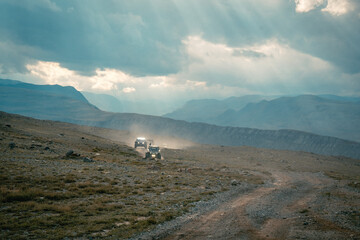 Obraz premium Buggy trip in a Altai desert. Mountain landscape with hills and beautiful blue sky with clouds in background. Off-road vehicles driving on a dust dirt road. Active leisure in Altai Republic.