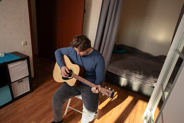 Focused Man Practicing Acoustic Guitar at Home, musician studying chords for performance, improving...