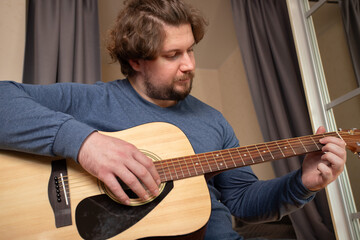 Obraz premium Man Practicing Guitar in Cozy Bedroom, guitarist embracing melody and rhythm