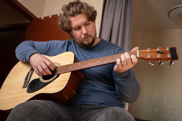 Obraz premium Man Practicing Acoustic Guitar at Home, hobby of strumming acoustic guitar, learning classic chords