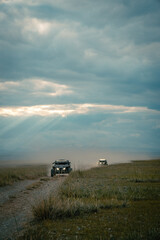 Fototapeta premium Buggy trip in a Altai desert. Mountain landscape with hills and beautiful blue sky with clouds in background. Off-road vehicles driving on a dust dirt road. Active leisure in Altai Republic.