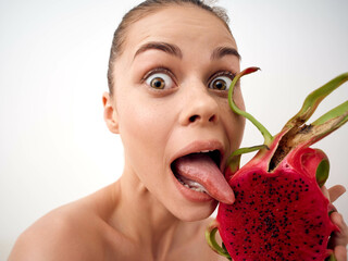 Cheerful woman playfully sticking out her tongue while holding a vibrant dragon fruit in front of her face