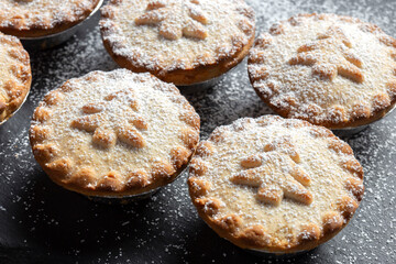 Homemade mince pies dusted with icing sugar on a slate board. Christmas festive cooking concept.
