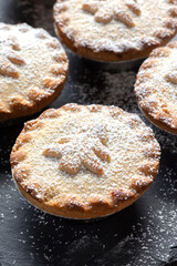 Homemade mince pies dusted with icing sugar on a slate board. Christmas festive cooking concept.