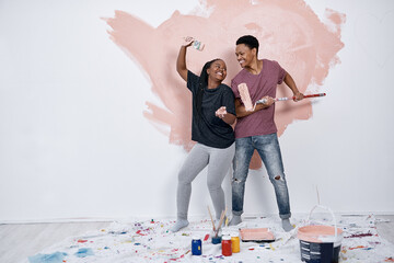 Black couple, painting fun and wall in home with renovation, love and bonding with art. Paint...