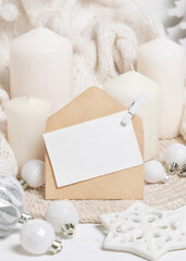 Card and envelope near white sweater, pillar candles and Christmas decor, mockup