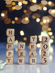 Small wooden blocks with the text Happy New Year 2025 against a blurred Christmas lights background