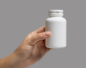 Female hand holding a white plastic pill bottle closeup against grey, Healthcare concept