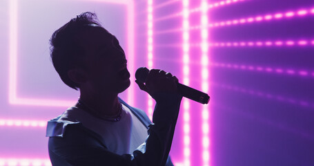 Naklejka premium Pop Concert with a Romantic Atmosphere: Young Talented Musician Performing Live on Stage in Front of Screen with Pink Visual Effects. Creative Cinematic Footage with Singer's Silhouette