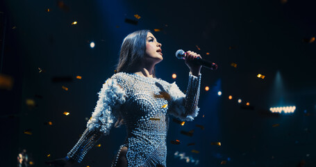 Portrait of a Female Artist Passionately Performing an Emotional Song on Stage. Musician Wearing a Creative Outfit, Holding a Microphone, Glittering Confetti Falling Down, Reflecting Dramatic Lights
