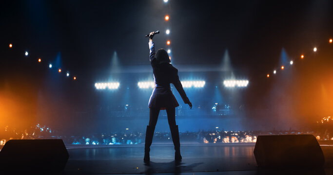 Music Contest: Back View of a Pop Music Artist Performing a Hit Song on Stage in Front of a Sold-Out Audience. Her Charismatic Stage Presence and Lyrics Electrify the Diverse Music Fans
