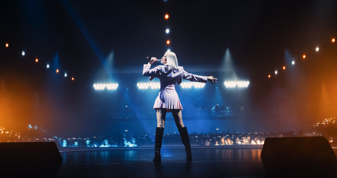 Music Contest: Back View of a Pop Music Artist Performing a Hit Song on Stage in Front of a Sold-Out Audience. Her Charismatic Stage Presence and Lyrics Electrify the Diverse Music Fans