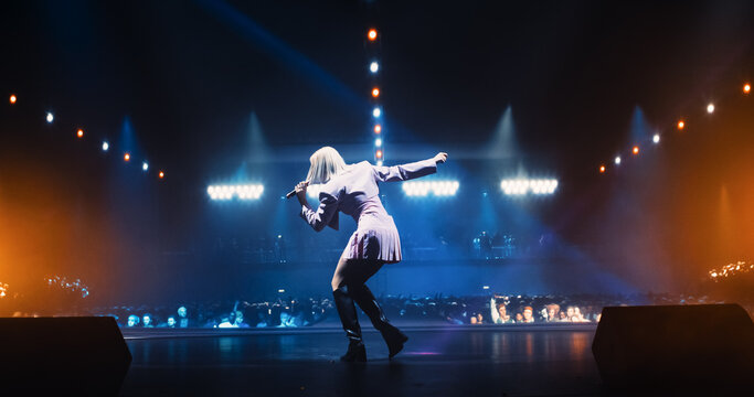 Music Contest: Back View of a Pop Music Artist Performing a Hit Song on Stage in Front of a Sold-Out Audience. Her Charismatic Stage Presence and Lyrics Electrify the Diverse Music Fans - Powered by Adobe