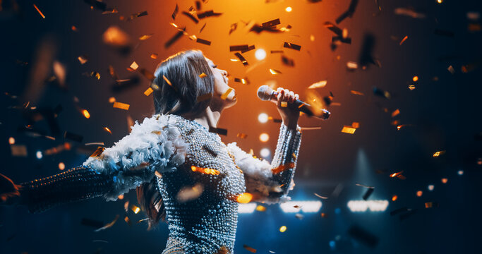Portrait of a Female Artist Passionately Performing an Emotional Song on Stage. Musician Wearing a Creative Outfit, Holding a Microphone, Glittering Confetti Falling Down, Reflecting Dramatic Lights
