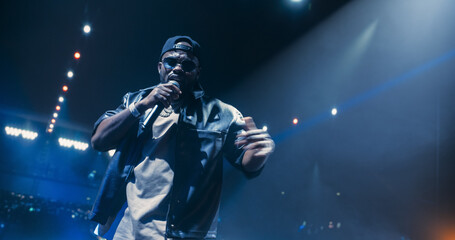 Naklejka premium Portrait of a Male Rapper Singing an Emotional Song. Spectacular Concert with a Talented Hip Hop Star. His Soulful Voice and Catchy Tunes Keep the Audience Vibing to the Sounds of Modern Music