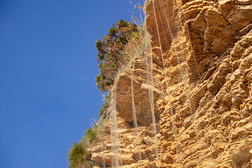 Obraz premium Protective netting securing a cliff face from rockfalls under blue sky