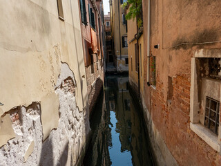 A narrow canal in Venice, Italy, lined with weathered buildings.