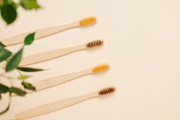 Biodegradable bamboo toothbrushes with green leaves on beige background with copy space, top view