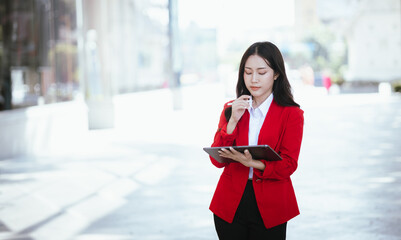 Confident Asian businesswoman standing in a modern city with a smile while using a smartphone. She is dressed professionally.