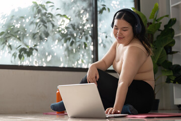 Woman in Activewear Enjoying Music While Using Laptop at Home with Greenery in Background