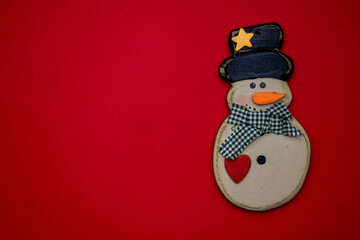 Festive snowman decoration with a black top hat and scarf against a bright red background during the holiday season