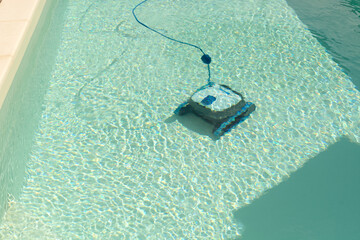 The robot pool cleaner cleans the bottom of the pool with clean water on a sunny summer day. The concept of cleaning swimming pools in hotels, resorts and country houses.