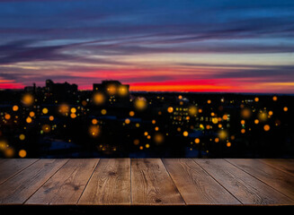 Background. Backdrop. An empty wooden table against the background of the night city. Sunset. Wooden surface. The urban landscape. The lights of the night city.  Light in the window, defocus lights.