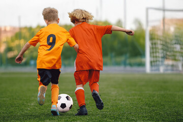 Happy Children Play Soccer Ball on Grass Pitch. Kids in Red and Orange Football Teams in Match. Boys Soccer Teams Competing For The Ball During A Football Match. Kids Play Sports In the Stadium