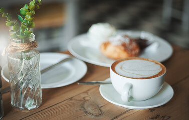 Coffee shop, morning and cappuccino at table with food, pastry and breakfast at cafe with minimalist decor. Venue, plate and afternoon tea with latte, mug and cream with hot drink and French diner