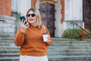 Upset sad, skeptical, serious woman holding smartphone gadget for communicate outdoors. Negative people emotion, Urban lifestyle concept. Angry 30s girl with paper cup of coffee reading bad news