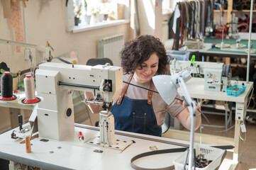 A woman tanner sews a leather belt on a sewing machine. 