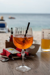 A glass of Aperol on the beach in Croatia, with a scenic backdrop of the sparkling sea and sandy shore.