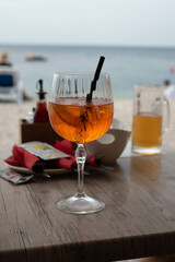 A glass of Aperol on the beach in Croatia, with a scenic backdrop of the sparkling sea and sandy shore.