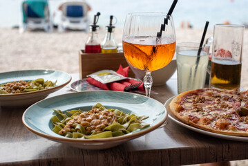 unch by the sea in Croatia, featuring a glass of Aperol, green spaghetti with shrimp, and pizza against a beautiful sea view.