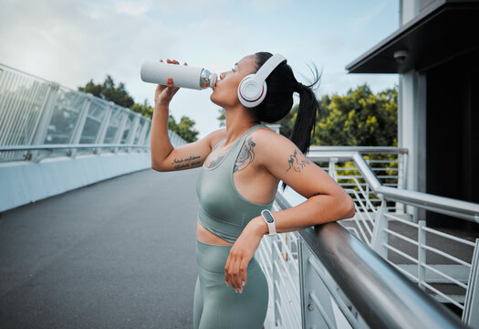 Woman, headphones and drinking water outdoor for fitness, exercise and health with bottle and workout. Athlete, music and challenge in city for training, streaming and drink with healthy cardio run